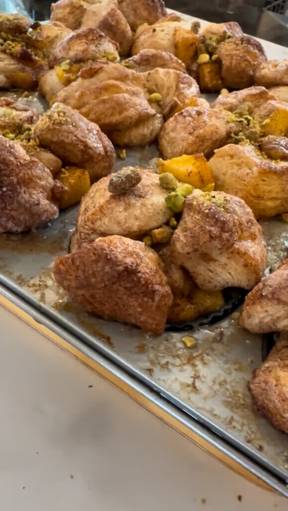 Close-up of freshly baked mini mango monkey breads in a muffin tin, topped with chopped pistachios.