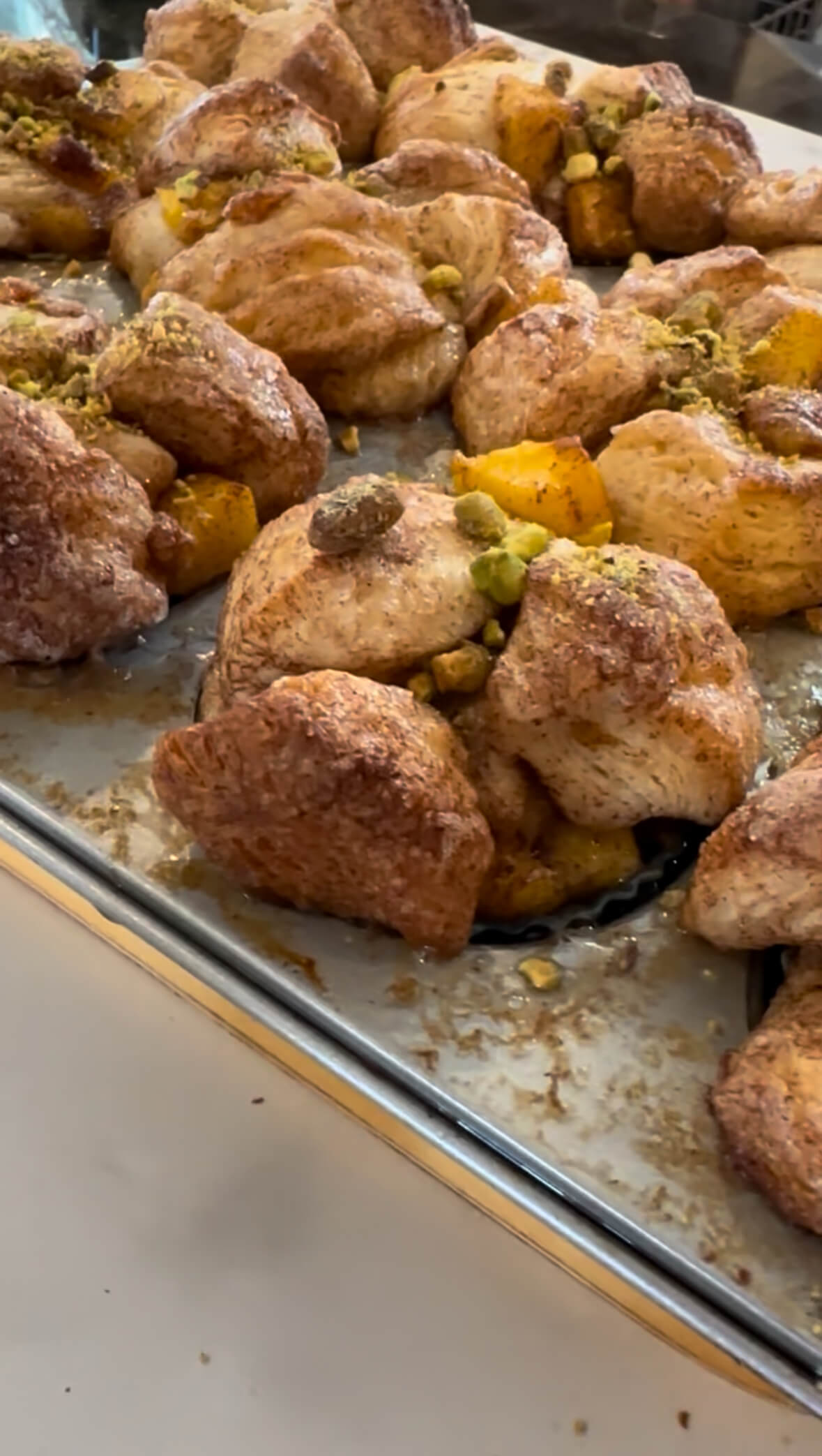 Close-up of freshly baked mini mango monkey breads in a muffin tin, topped with chopped pistachios.